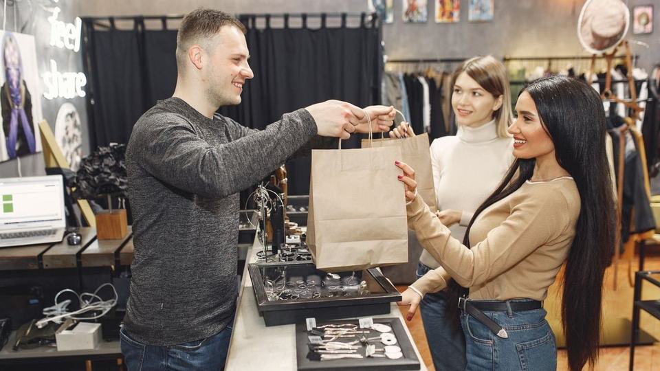 Shop assistant handing a paper bag to smiling customers across the counter